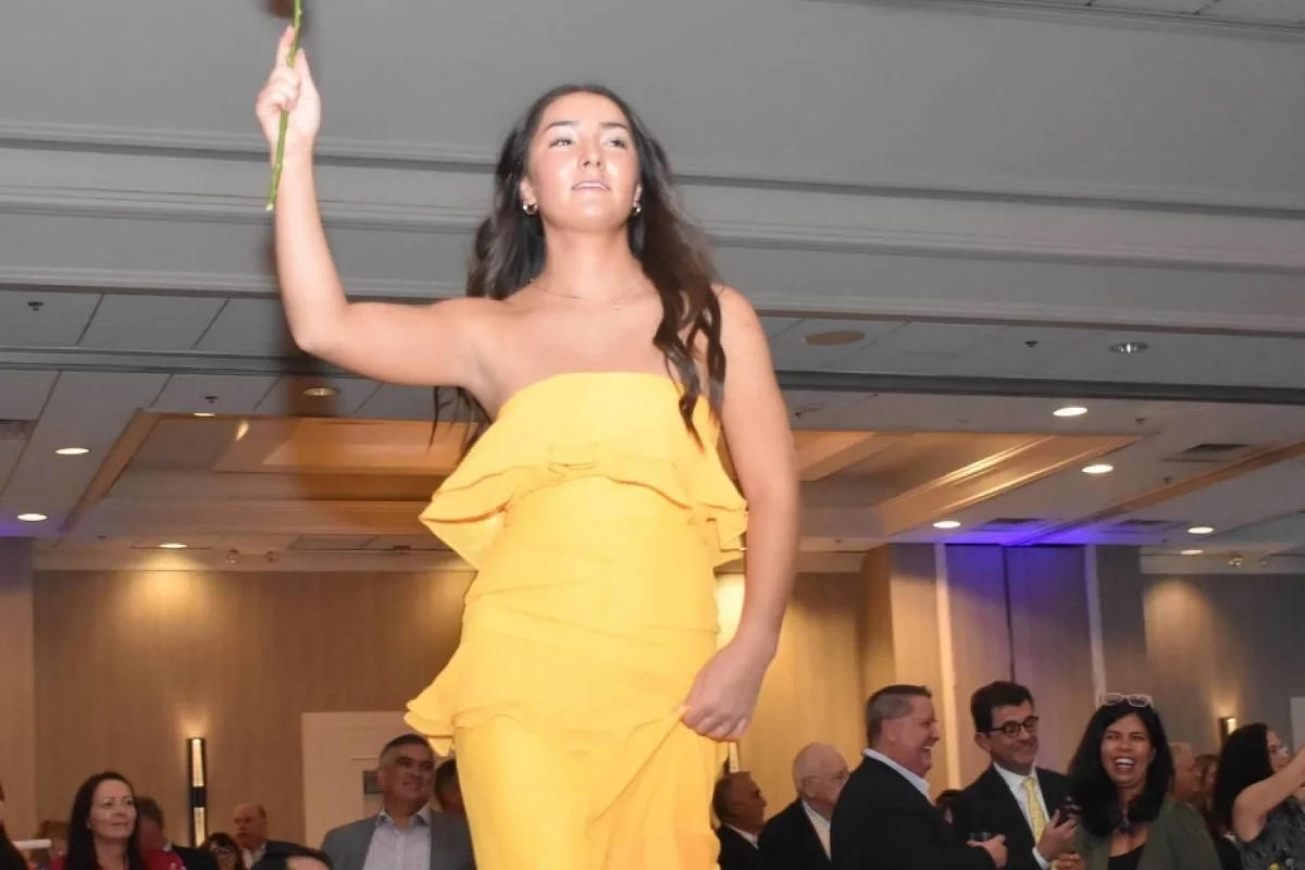 student in yellow dress holding up a rose